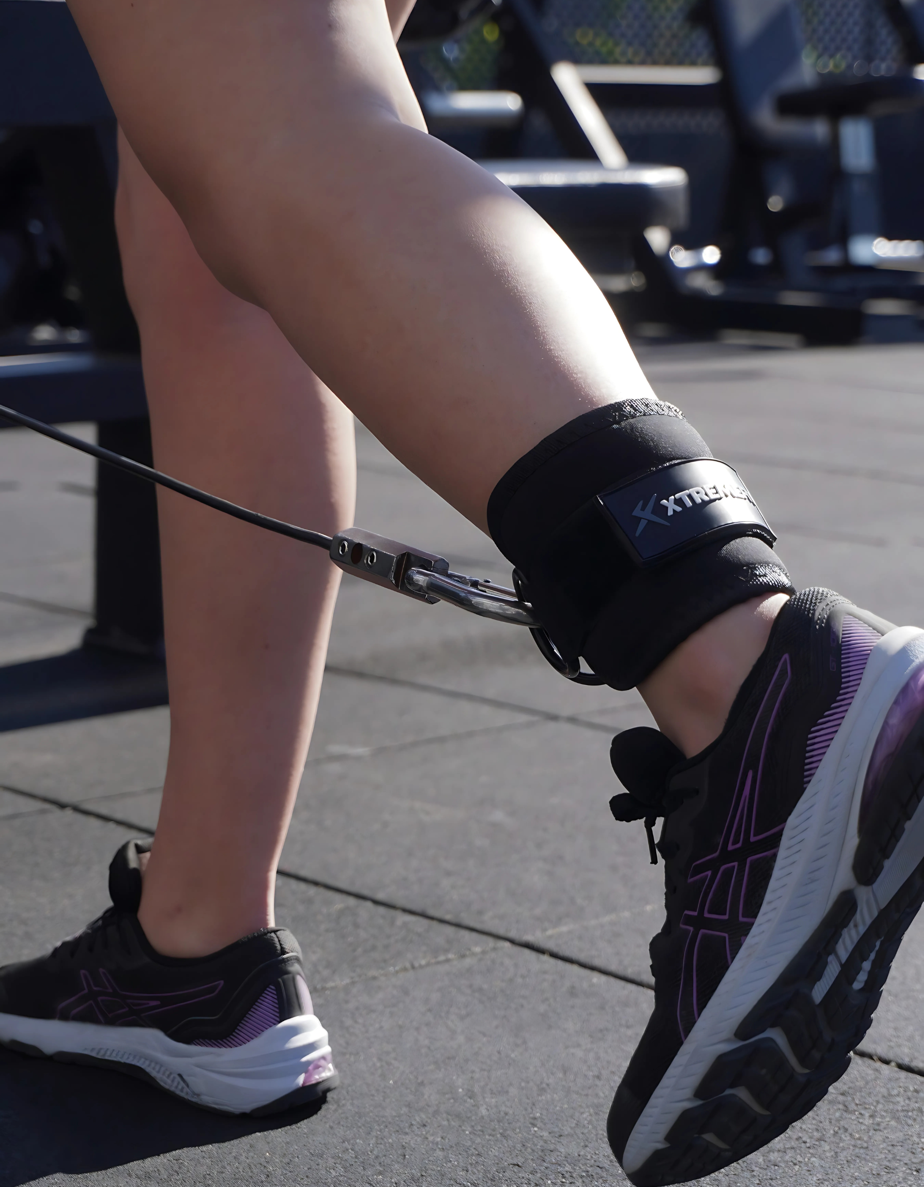 Athlète en salle de muscu qui fait un exercice bas du corps avec les sangles de chevilles noir xtremefit de haute qualité