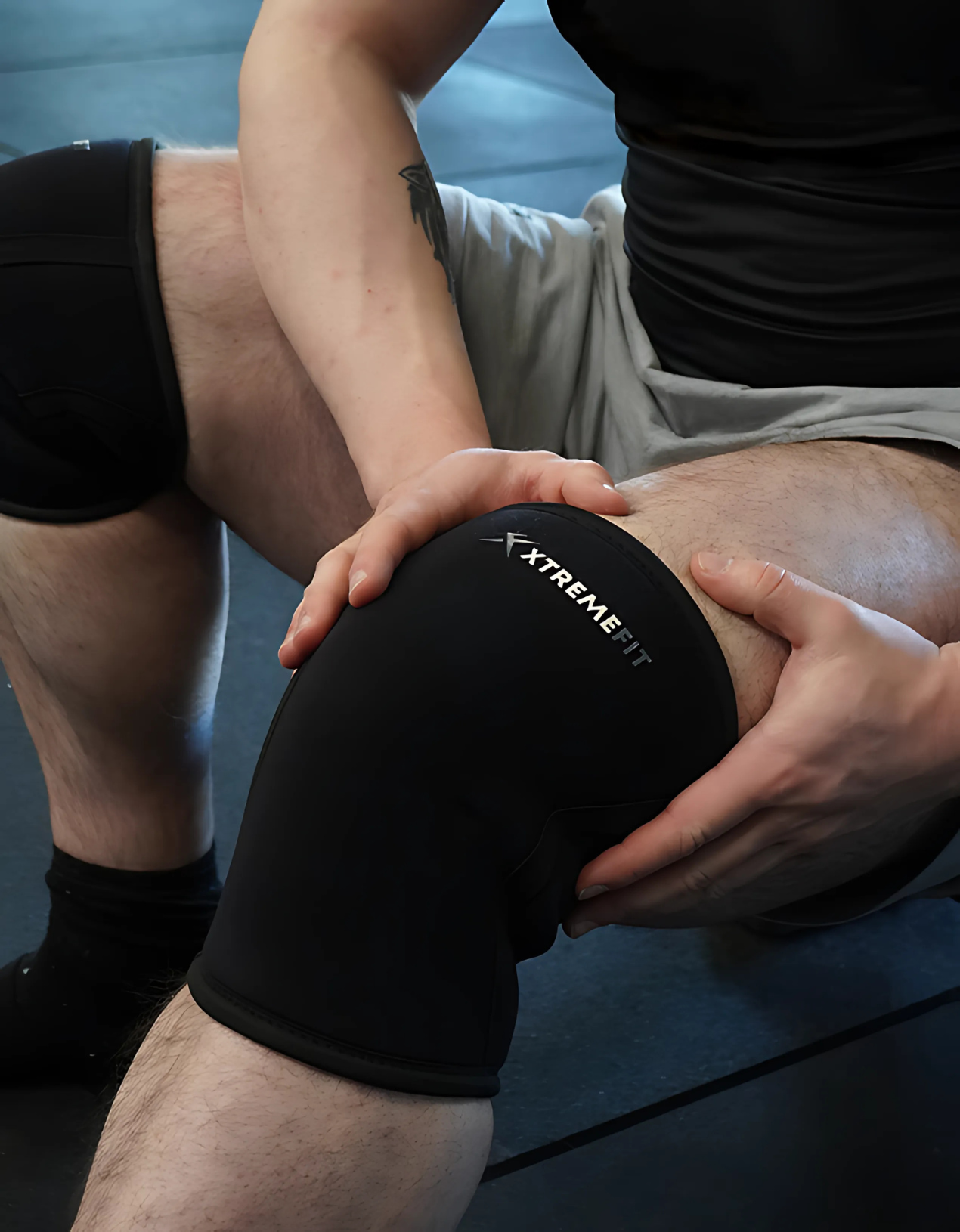 Athlète assis avec des genouillères de musculation / force xtremefit noir en néoprène 7mm